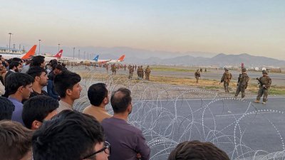 在喀布尔国际机场内，周一仍聚集大批想要逃离阿富汗的平民（左），全副武装的美军持枪在停机坪维持秩序。（法新社）