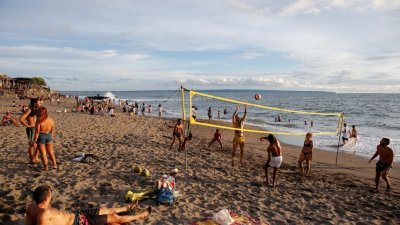 图为12月2日在峇厘岛的长谷海滩，游客在沙滩上玩球观赏日落，有者下海戏水。（图取自路透社）