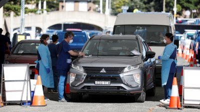 随著变种病毒Omicron在澳洲悉尼继续传播，医护人员周四忙著替车龙中的民众进行“得来速”（Drive-thru）新冠肺炎病毒检测。（图取自路透社）