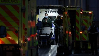 在英国皇家伦敦医院外，停放了一排的救护车，其中一辆救护车上的人员忙著工作。（图取自法新社）