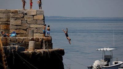 热浪近日侵袭北美，群众各出奇招消暑。图为马萨诸塞州的年轻人跳入海中玩水。（图取自路透社）