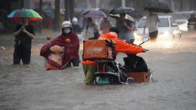 中国河南省郑州周二下午4时至5时一小时降水量达201.9毫米，单小时降雨量超过日历史极值，降雨强度历史罕见。图为当天傍晚人们在暴雨中趟水前行。(图取自中新社)