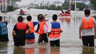 河南省部分地区，仍然受暴雨引发的洪水影响。图为救援人员周日在河南新乡的小朱庄协助灾民撤离。（图取自中新社）