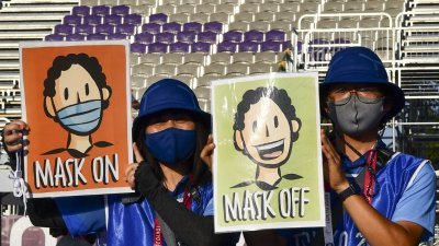 东京奥运会工作人员在赛场上拿著画报，提醒在场人士戴口罩防疫。（图取自路透社）