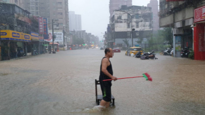 台北市民在泥泞水中行走，拿扫把准备清理环境。（图取自中央社/台北市政府提供）