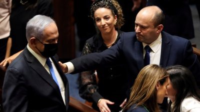 在国会投票通过新政府任命后，统治以色列长达12年的内塔尼亚胡表情凝重，而其继任者贝内特则拍其肩膀，似在安慰他。（图取自路透社）