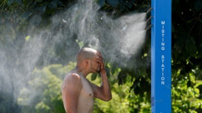 在不列颠哥伦比亚省，一名男子在雾气站降温。（图取自路透社）