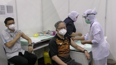 陈家兴（前排左起）和李文材卷起衣袖，准备让医护人员注射疫苗。