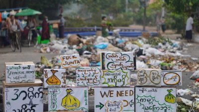 缅甸公民不服从运动周二发起“垃圾罢工”，并在仰光堆满垃圾的街道旁竖起抗议军政府的标语牌子。（第三方供应/路透社）