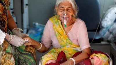 在艾哈迈达巴德一家医院外等候入院治疗的80岁新冠肺炎患者，在医院外的救护车上暂靠吸氧协助呼吸。（图取自路透社）