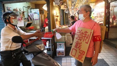 台湾周六新增180宗新冠肺炎本土病例，其中43宗集中于台北市万华地区。位于万华区三水街的市场工作人员当天上午背著防疫看板，为出入的民众喷洒酒精进行手部消毒。（图取自中央社）