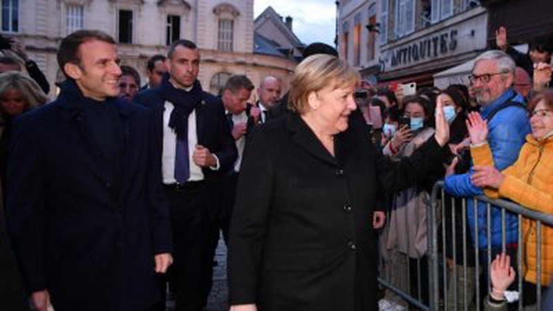 法国总统马克龙（左）与德国看守总理默克尔（右）在博讷的街道上漫步，并和沿途民众交流。（图取自法新社）