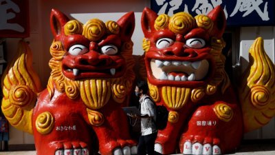 在冲绳县首府那霸国际大道上，一名戴著口罩的男子走过冲绳守护兽狮子狗Shisa雕像前。-路透社-