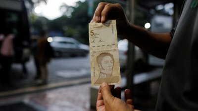 委内瑞拉一名男子周五在首都加拉加斯，出示一张5玻利瓦尔新钞。（图取自路透社）