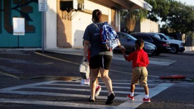 在美国佛罗里达州，一名母亲拖著孩子去学校上课。（图取自路透社）