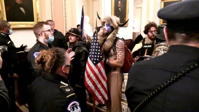 今年1月6日，钱斯利赤裸刺有大量纹身的上半身，戴著有角的头饰，拿著扩音器和美国国旗，在国会里与警察对峙。（图取自路透社）