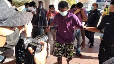 身穿紫色带领T恤、黑底绿条纹花色短裤的被告基汝巴卡然（中）被警方押到法庭时，坦然面对媒体的镜头。
