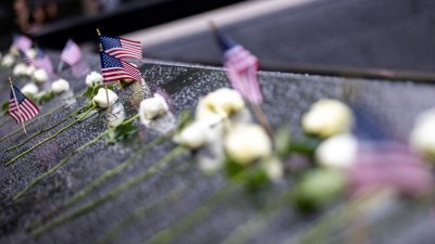 911恐袭20周年前夕，民众在纽约市世贸中心遗址的反射池边留下鲜花和国旗，悼念逝者。（图取自路透社）