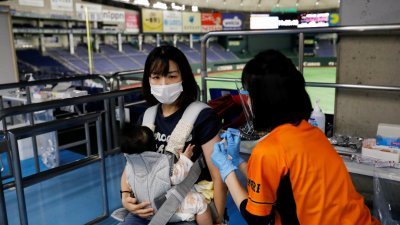 美国总人口是日本的2.6倍，但日本目前每天接种超过100万剂新冠疫苗，较美国多打约30万剂。一名日本妈妈近日在东京巨蛋体育馆进行疫苗施打。（图取自路透社）