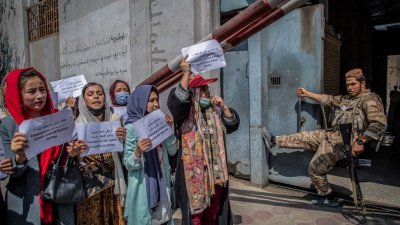 一群妇女周日在喀布尔前妇女事务部前抗议，要求妇女享有更好的权利，而一旁则有一名塔利班分子看著。（图取自法新社）