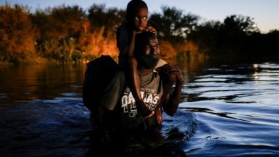 海地移民让孩子骑在肩膀上，冒险涉水从墨西哥渡过里奥格兰德河，前往美国得州的德尔里奥。（图取自路透社）