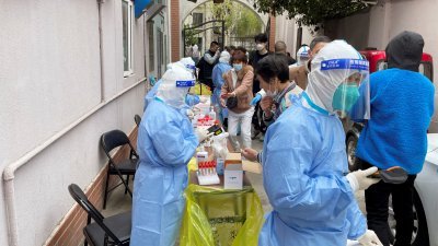 身穿防护服的医护人员，在上海的一个小区内，为居民进行核酸检测。（图取自路透社）