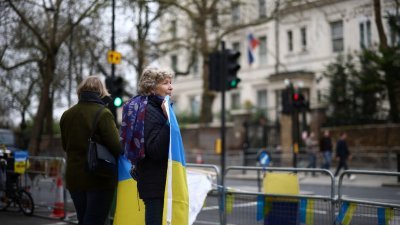 两名妇女日前在俄罗斯驻英大使馆对面，举起乌克兰国旗抗议俄军入侵乌国。（图取自路透社）