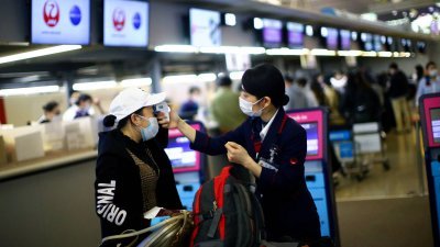 日本航空一名工作人员，在大阪的关西国际机场，为旅客测量体温。（路透社档案照）