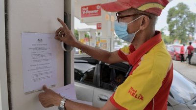 一名油站员工在油站外，张贴告示，提醒外国注册交通工具不能添购RON95补贴汽油。（图取自马新社）