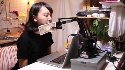 日本无用小物发明家藤原麻里菜近日发表新作“钞票搧脸机”，希望能替上班族找回努力工作的动力。 （图截取自影片）
