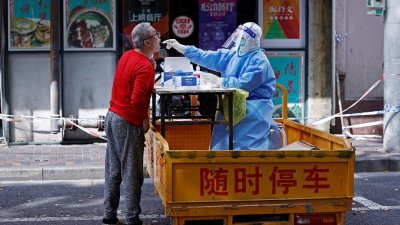 上海疫情防控期间，一名身穿防护服的医护人员对居民进行核酸检测。（图取自路透社）