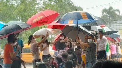 学生家长排成两排，撑伞遮学生过马路坐上学生巴士。