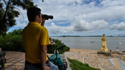 台海局势紧张升级之际，周三在中国厦门环岛东路海边，一名男子通过双筒望远镜观察天空。（图取自法新社）
