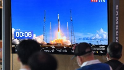 在首尔的一个火车站，人们周五观看载有韩国探月器的美国“猎鹰9”号运载火箭发射升空的实况直播画面。（图取自法新社）