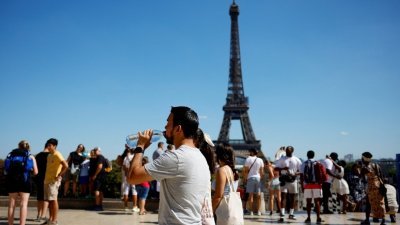 欧洲热浪袭来，法国巴黎名胜地艾菲尔铁塔前，有民众饮水补充流失水分。（图取自路透社）