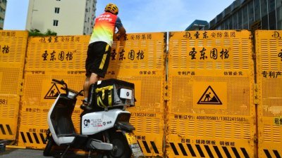随著疫情升温和防止病毒扩撒，中国海南省三亚市在上周六封城，一名快递员站在电动脚踏车上将物品送进围栏内。（图取自《中国日报》/路透社）