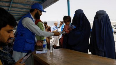 一名流离失所的阿富汗妇女于今年7月28日，在喀布尔的流离失所者现金援助分配中心从WSTA员工手中领取现金援助。（图取自路透社）