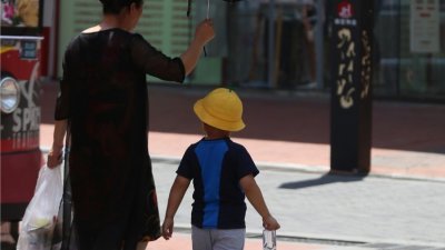 在中国重庆街头，有大人在炎热的天气下为小孩撑伞遮阳出行。（图取自中新社）