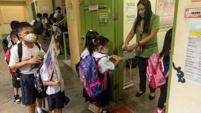 在菲律宾八打雁省圣胡安市的一所学校，周一开学日，一名教师对进班的学生双手喷洒洗手液消毒。（图取自路透社）