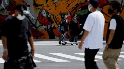 在日本东京街头，身穿和服的女性戴著口罩在十字路口行走。（图取自路透社）