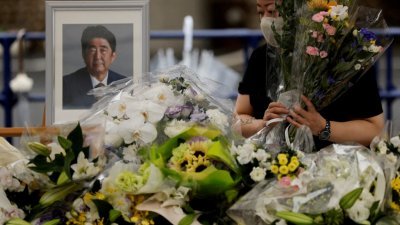 日本前首相安倍晋三7月8日遭枪杀身亡，一名哀悼者于上月15日在东京自民党总部，在安倍遗照旁边献花。（图取自路透社档案照）