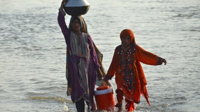 在俾路支省贾法拉巴德区的Sohbatpur地区，受洪水影响的妇女在从洪水袭击的家中逃离后，周日将饮用水装在容器中。（图取自法新社）