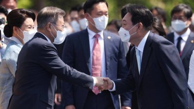 在尹锡悦（右）今年5月10日宣誓就职韩国总统的典礼上，他与前任文在寅握手问好。（图取自路透社档案照）