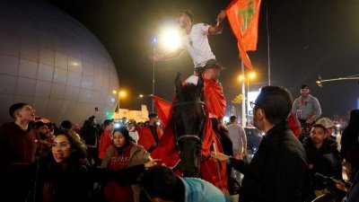 在摩洛哥的卡萨布兰卡，身披摩洛哥国旗的球迷庆祝球队在世界杯8强赛击败葡萄牙的壮举。（路透社）