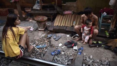 据泰国国家经济社会委员会统计，2021年泰国有810万贫穷人口，他们缺乏管道获得适当教育、健康、生活品质和金融等资源，另有28万个孩童因为贫穷而辍学。图为曼谷市区的一个贫民区，居民坐在棚屋外的铁轨上。（法新社档案照）