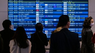 在日本东京羽田国际机场，人们周三站在航班抵达讯息公告牌前等候。（图取自法新社）