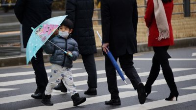 图为上月25日在首尔，一名戴著口罩的小男孩撑伞过斑马线的档案照。（图取自路透社）