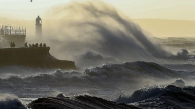 “尤尼斯”风暴周五袭击英国和爱尔兰，图为在威尔士南部的波斯考尔，人们聚集在海堤上观看海浪。（图取自法新社）