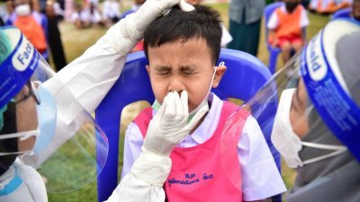 泰国陶公府的学校因疫情关闭一年后日前重新开学，卫生官员在开学第一天对教师和学生进行病毒检测。（图取自法新社）