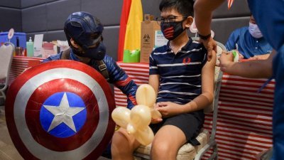 图为菲律宾马尼拉郊区塔吉格市，一名儿童在一家商场接受首剂辉瑞疫苗，一名打扮成美国队长的男子陪伴在他身边。（图取自路透社）